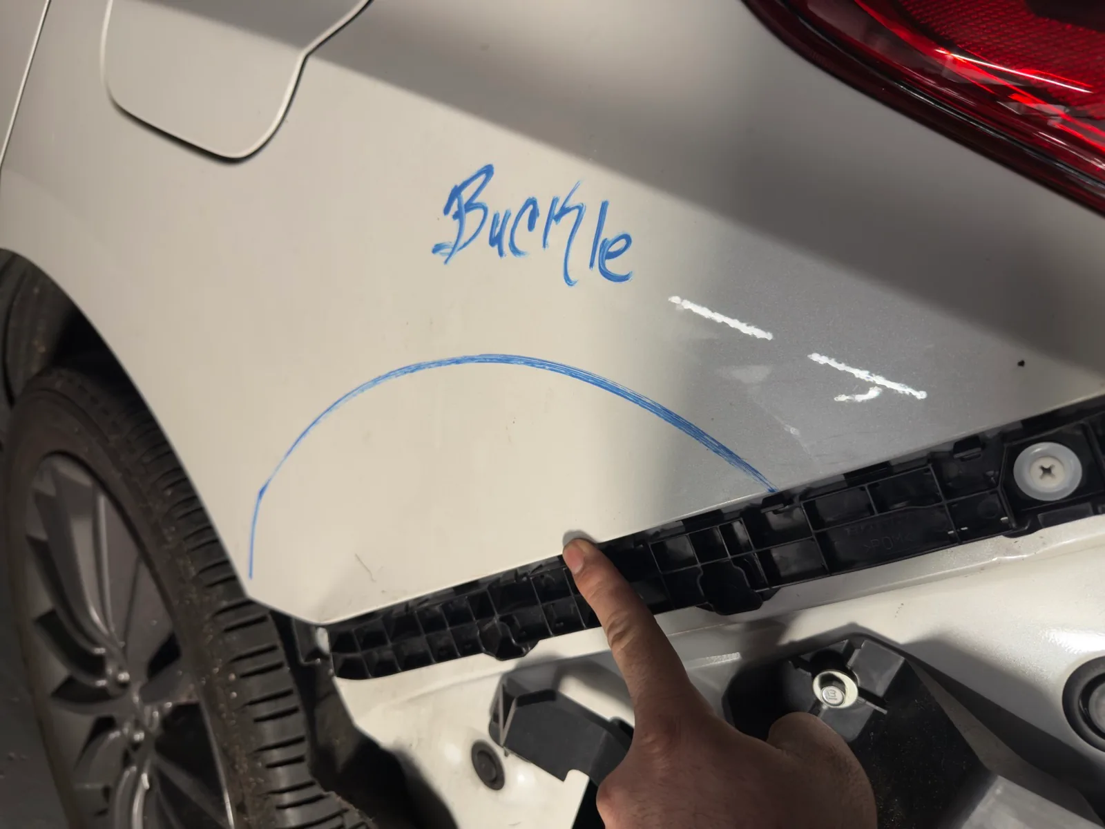 Technician marking a buckled white quarter panel in blue while writing an estimate at Exclusive Collision & Repair in Brooklyn, NY
