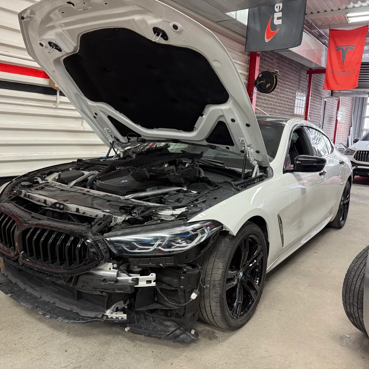 White BMW 8 Series Gran Coupe with the hood raised and the front bumper and grille removed, exposing the radiator support and front structural rails at Exclusive Collision & Repair in Brooklyn, NY