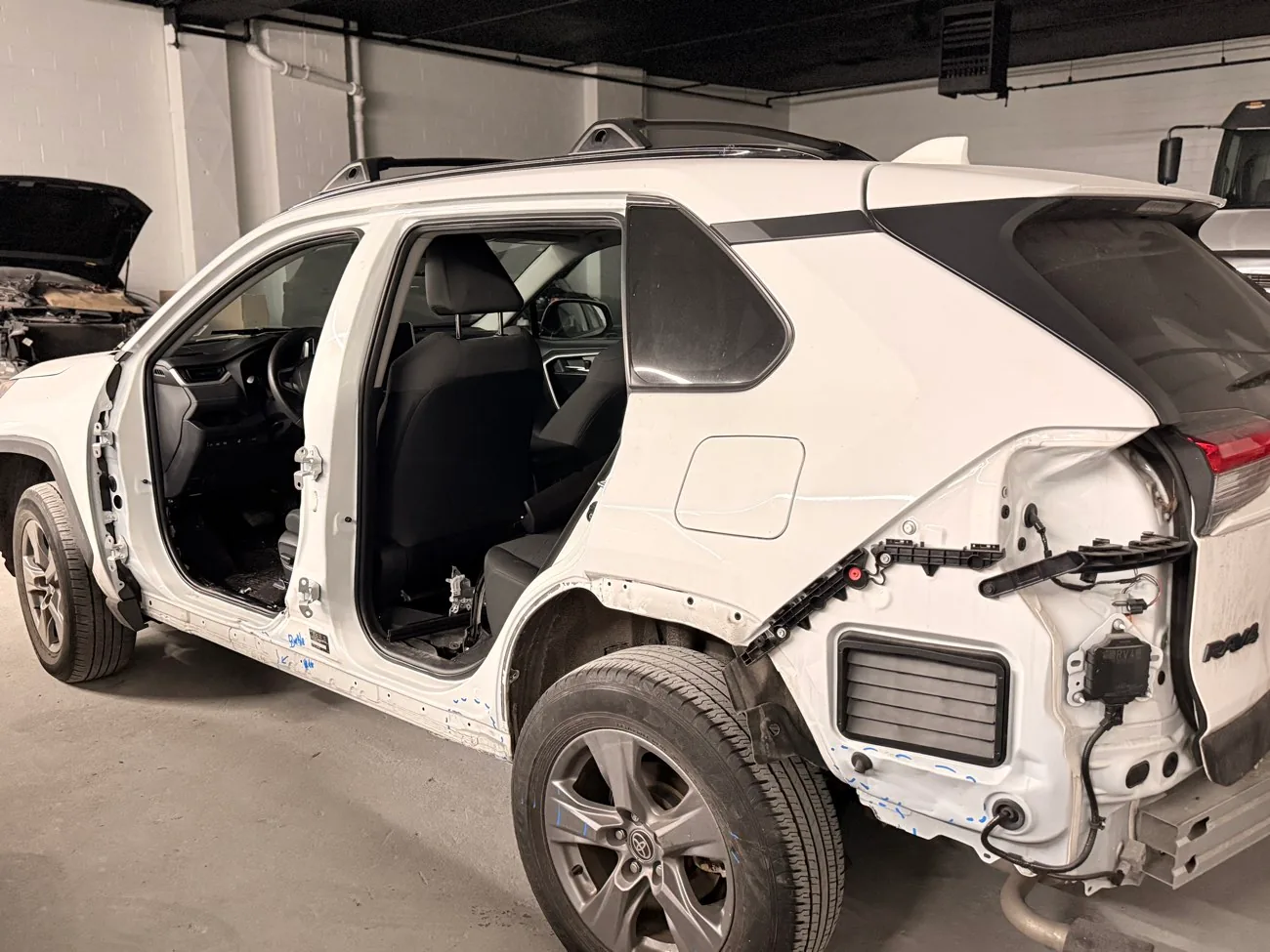 White Toyota RAV4 with both driver-side doors off and the rear quarter panel stripped, marked up in blue for unibody measurement during automotive frame repair at Exclusive Collision & Repair in Brooklyn, NY