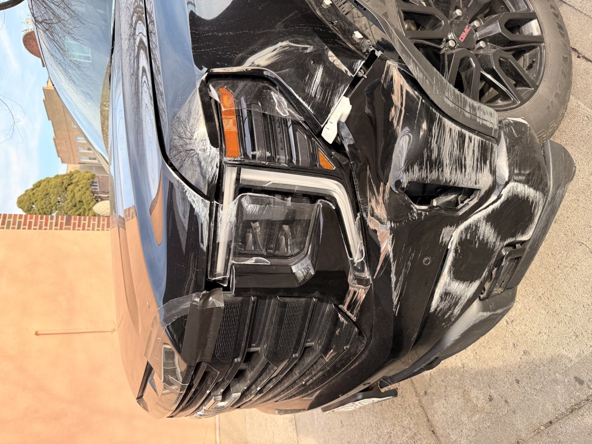 Black GMC Sierra pickup with front-end collision damage on a Brooklyn, NY street before being towed to Exclusive Collision & Repair