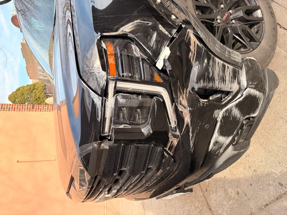 Black GMC Sierra pickup with front-end collision damage on a Brooklyn, NY street before being towed to Exclusive Collision & Repair